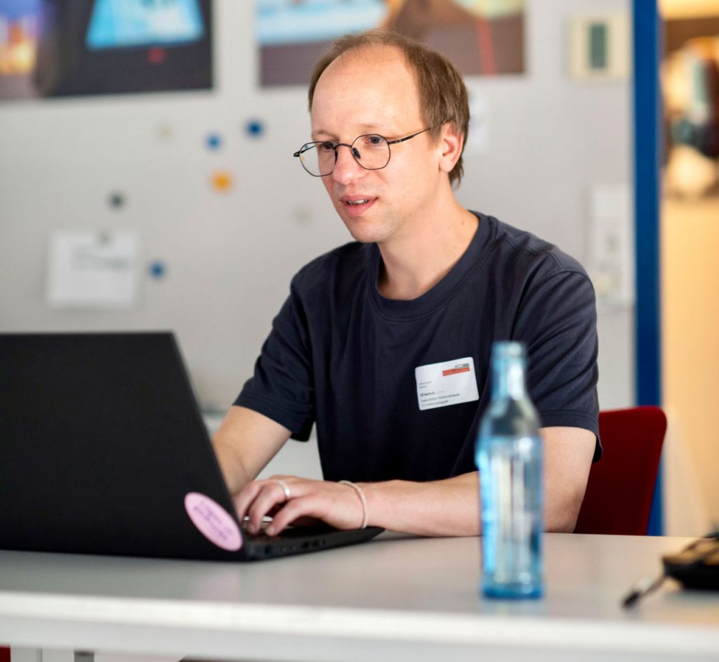 Till Neitsch sitzt an einem Tisch und arbeitet an einem Laptop.